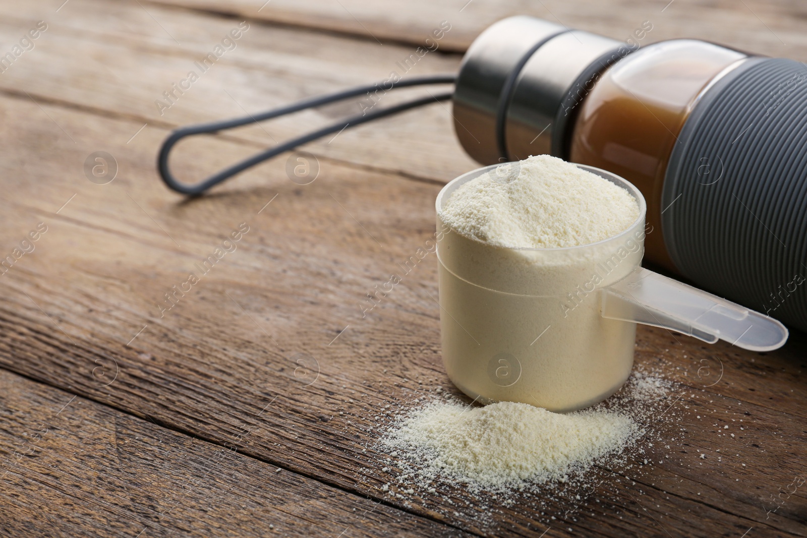 Photo of Measuring scoop of protein powder and bottle with shake on wooden table. Space for text