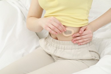 Photo of Woman applying contraceptive patch onto her belly on bed, closeup