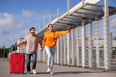 Photo of Being late. Couple with red suitcase running outdoors, space for text