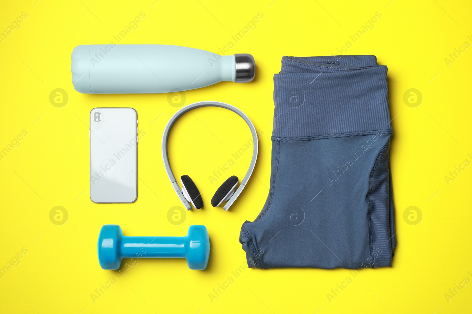 Photo of Stylish sports leggings, dumbbell, thermo bottle, headphones and smartphone on yellow background, flat lay