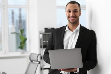 Smiling young businessman using laptop in office. Space for text
