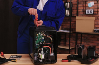 Photo of Repairman with screwdriver fixing coffee machine at table indoors, closeup