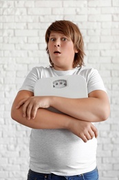 Photo of Emotional overweight boy with floor scales near white brick wall