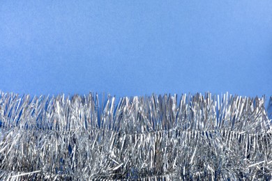 Photo of Silver tinsel on blue background, top view. Space for text