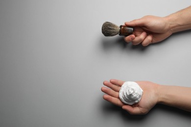 Photo of Man holding shaving foam and brush on light grey background, top view. Space for text
