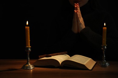 Photo of Woman praying at table with burning candles and Bible, closeup