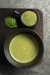 Photo of Cup of fresh matcha tea and green powder on grey table, top view