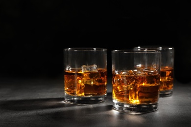 Photo of Golden whiskey in glasses with ice cubes on table. Space for text