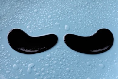 Photo of Black under eye patches on light blue wet background, closeup. Cosmetic product