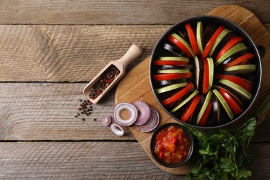 Photo of Cooking delicious ratatouille. Different fresh vegetables, scoop with spices and round baking pan on wooden table, flat lay. Space for text