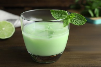 Photo of Delicious mint liqueur with green leaves on wooden table, closeup