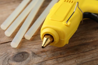 Yellow glue gun and sticks on wooden table, closeup