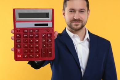 Photo of Happy accountant with calculator on yellow background, selective focus