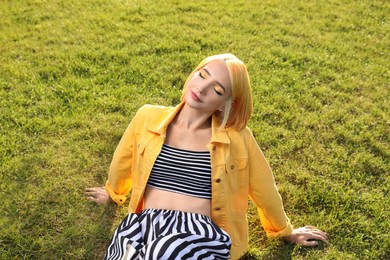 Photo of Beautiful young woman with bright dyed hair on green grass