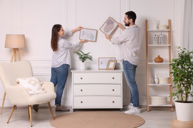 Photo of Man and woman hanging picture frames on white wall at home