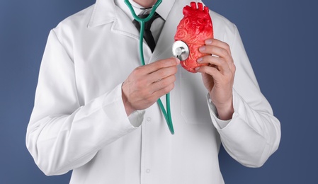 Photo of Doctor holding model of heart and stethoscope on color background. Prevent heart attack
