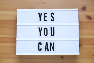 Photo of Lightbox with phrase Yes You Can on wooden table, top view. Motivational quote