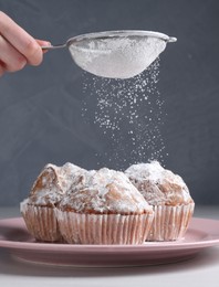 Photo of Woman with sieve sprinkling powdered sugar onto muffins at white wooden table, closeup