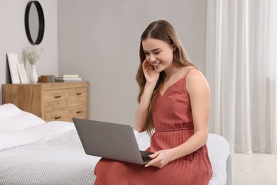 Photo of Happy woman with laptop on bed in bedroom