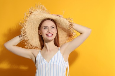 Beautiful young woman in straw hat on orange background, space for text