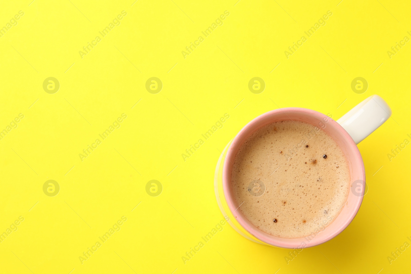 Photo of Aromatic coffee in cup on yellow background, top view. Space for text