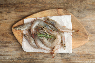 Photo of Fresh raw shrimps with rosemary on wooden table, top view