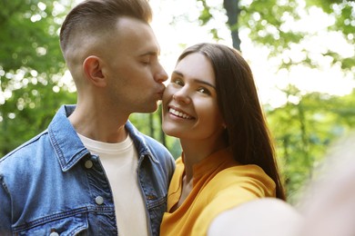 Photo of Affectionate young couple kissing and taking selfie outdoors