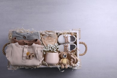 Photo of Wooden box with baby clothes, booties and toys on grey background, top view. Space for text