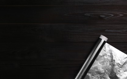 Photo of Roll of aluminum foil on dark wooden table, top view. Space for text