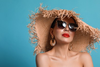 Photo of Attractive woman in fashionable sunglasses and wicker hat against light blue background. Space for text