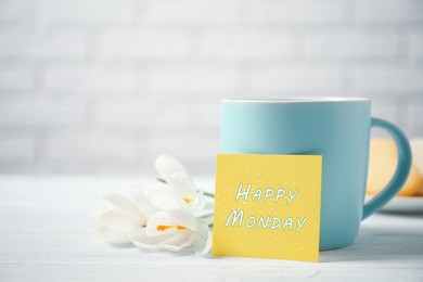 Image of Cup of hot drink, flowers and card with phrase Happy Monday on white wooden table, closeup 