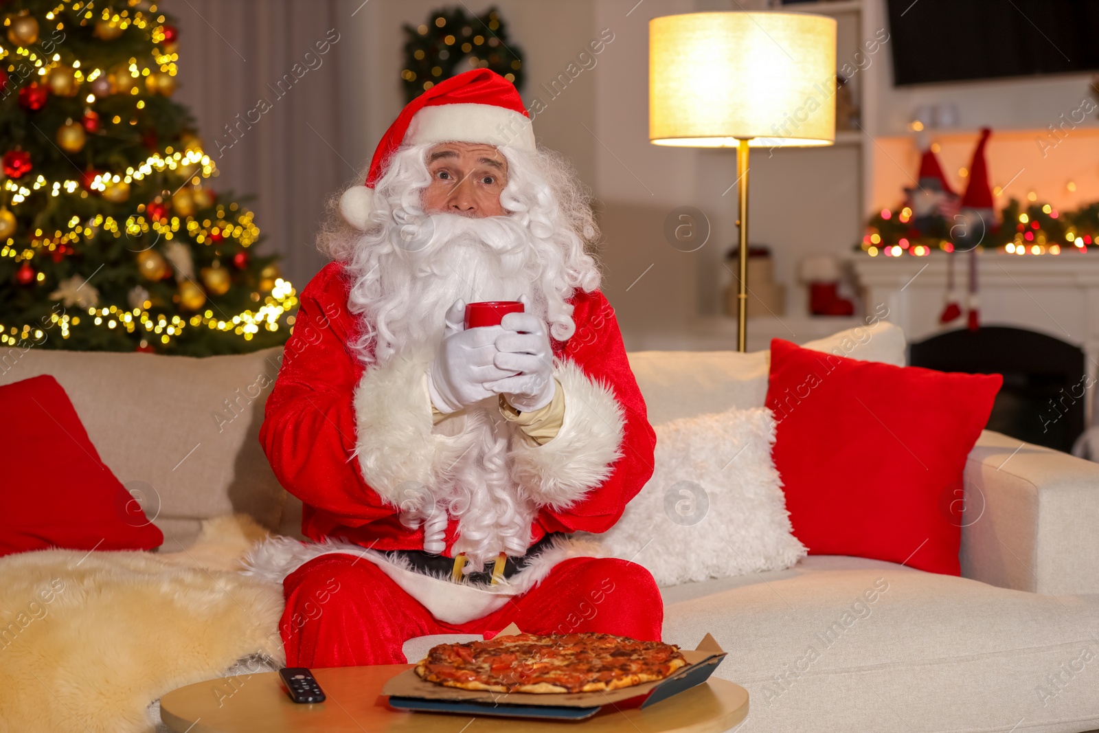 Photo of Merry Christmas. Santa Claus with cup of drink watching TV on sofa at home