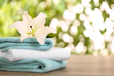 Photo of Stack of clean towels with lily on table against blurred background. Space for text