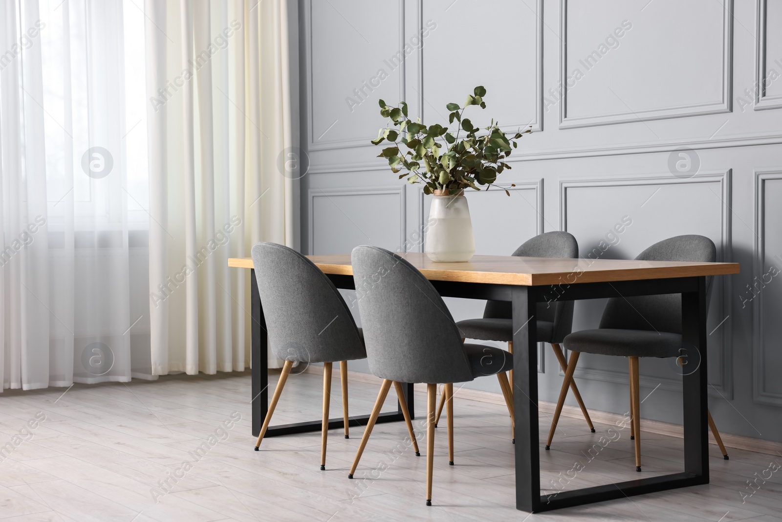 Photo of Soft chairs, table and vase with eucalyptus branches in stylish dining room