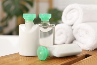 Photo of Wooden tray with mini bottles of cosmetic products and rolled towels on bath tub in bathroom, closeup