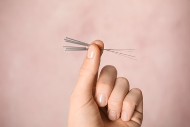 Photo of Woman holding needles for acupuncture on pink background, closeup