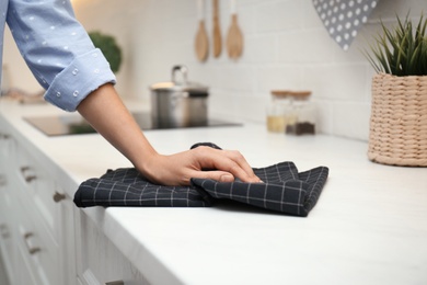 Photo of Woman wiping white table with kitchen towel, closeup