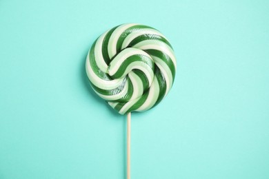 Photo of Stick with colorful lollipop swirl on turquoise background, top view