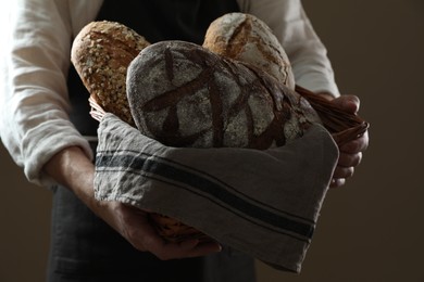 Photo of Man holding wicker basket with different types of bread on brown background, closeup