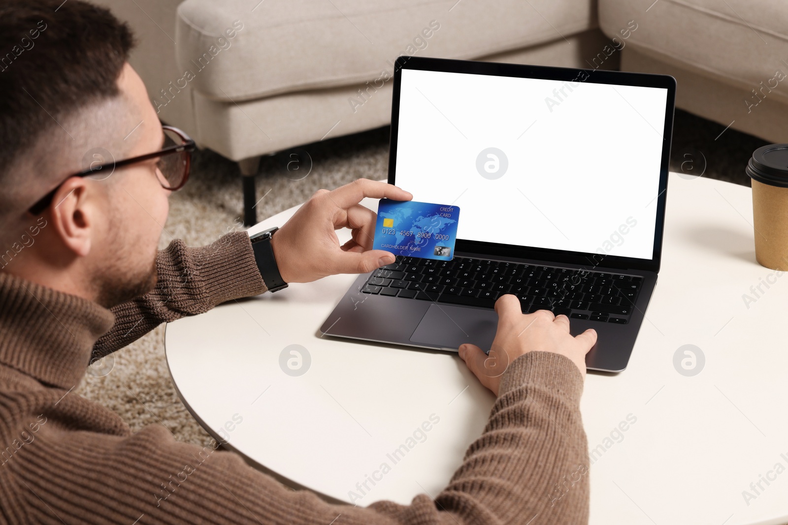 Photo of Man with credit card using laptop for online shopping at white table indoors, selective focus