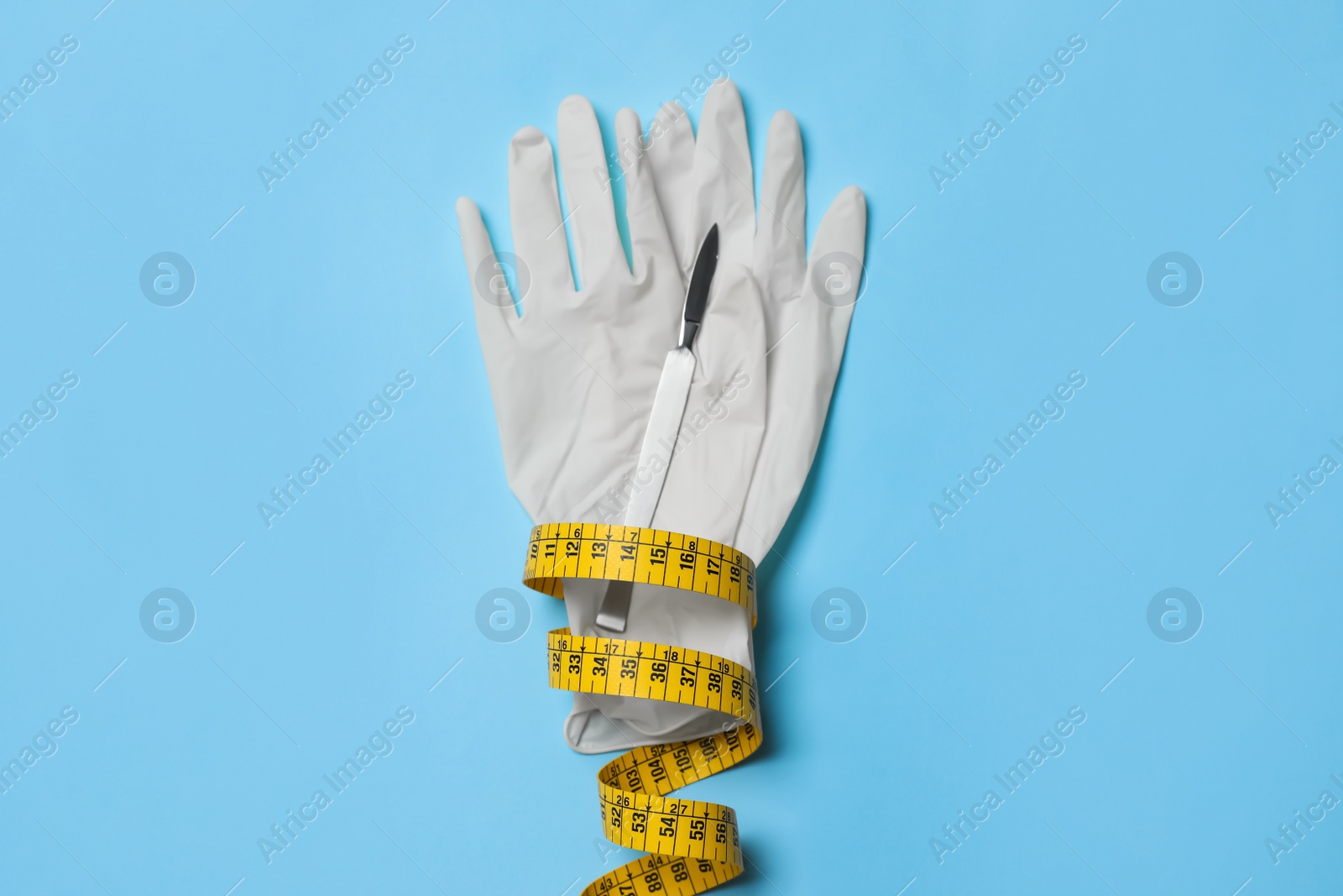 Photo of Scalpel, gloves and measuring tape on light blue background, top view. Weight loss surgery