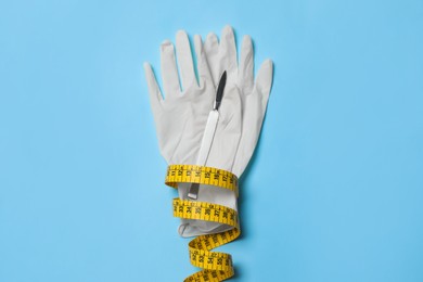 Photo of Scalpel, gloves and measuring tape on light blue background, top view. Weight loss surgery