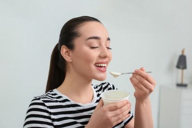 Photo of Happy woman eating tasty yogurt in room