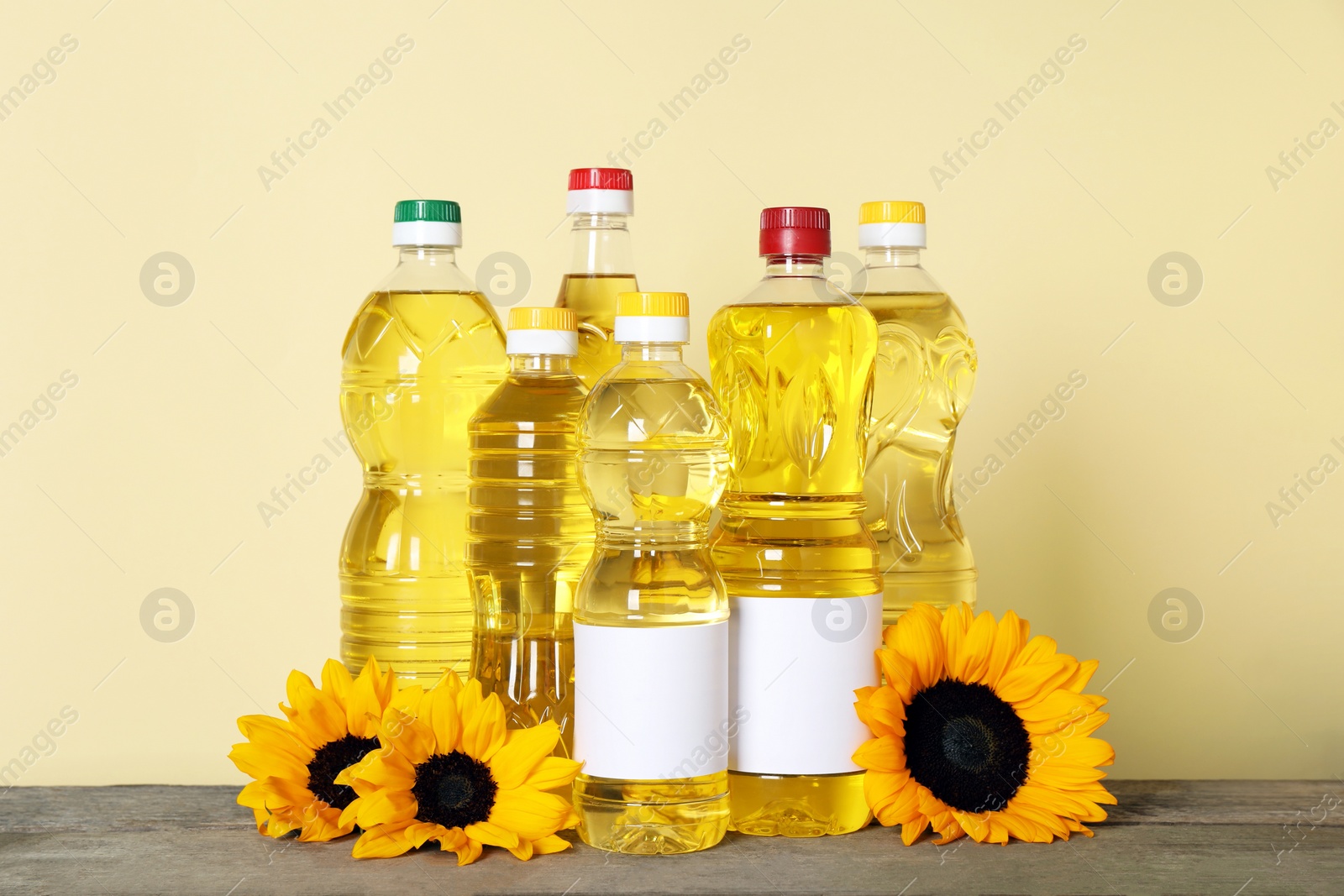 Photo of Bottles of cooking oil and sunflowers on wooden table