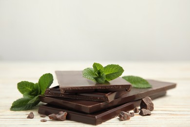 Photo of Tasty dark chocolate pieces with mint on white wooden table