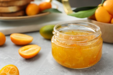 Photo of Delicious kumquat jam and fresh fruits on light grey marble table