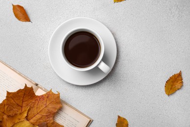 Photo of Cup of hot drink, book and autumn leaves on light grey textured table, flat lay