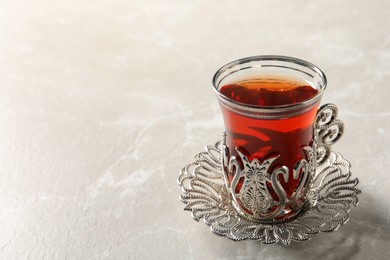 Photo of Glass of traditional Turkish tea in vintage holder on white marble table, closeup. Space for text