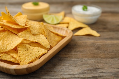 Photo of Plate of Mexican nacho chips on wooden table, closeup. Space for text