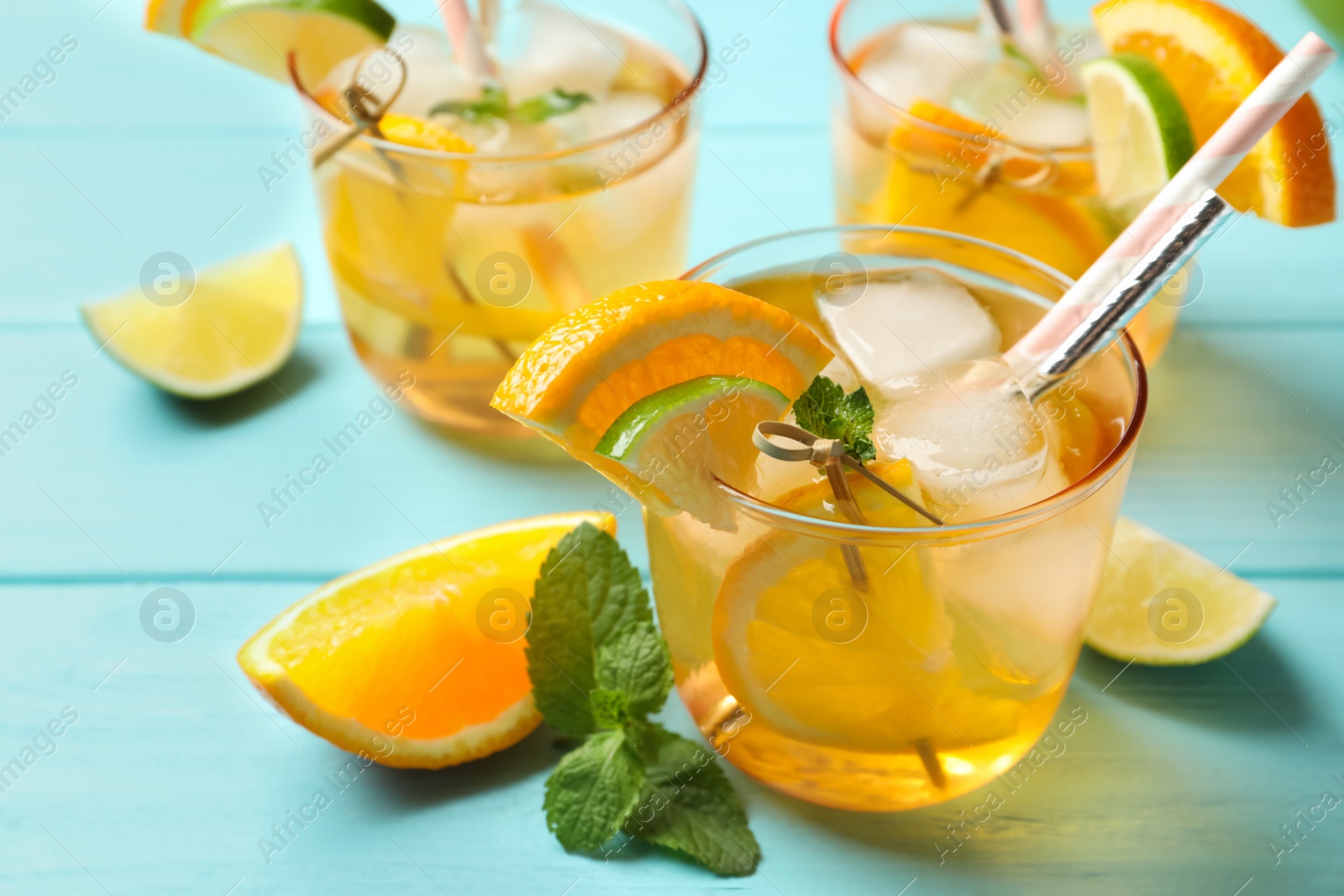 Photo of Delicious refreshing drink with orange and lime slices on light blue wooden table, closeup